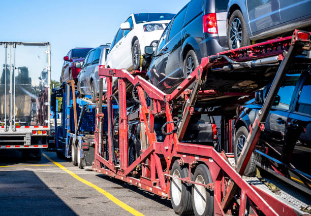 Big rig industrial grade professional car hauler semi truck with loaded cars on the two level hydraulic semi trailer standing on truck stop parking lot beside another semi trucks